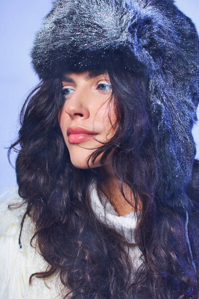 winter beauty, young woman in winter hat with snow and white sweater on grey backdrop, cool air