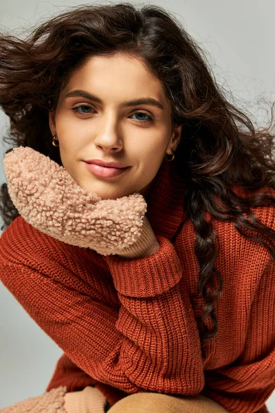 stock image wind blowing at face of curly pretty woman in terracotta sweater and mittens, winter fashion