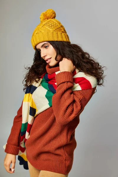 ストリップスカーフ付きボブル帽子と居心地の良いセーターでカーリーヘアのブルネット女性の肖像画 — ストック写真