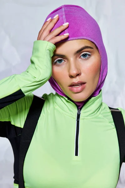 stock image portrait of pretty woman with blue eyes in warm ski mask posing with hand near face on grey backdrop