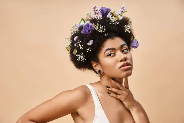 charming african american woman with colorful flowers in hair posing in lingerie on beige backdrop