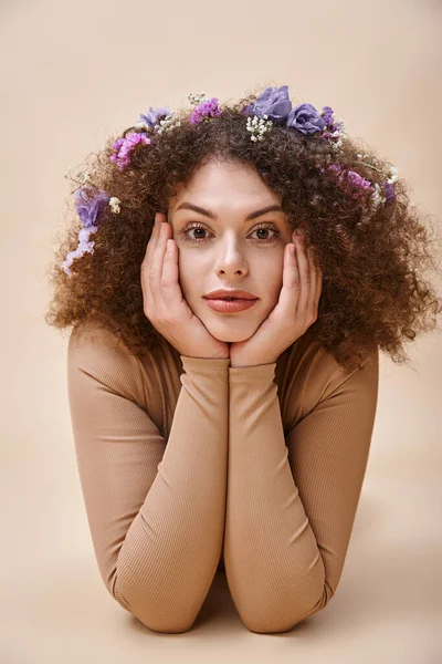 portrait of pretty and expressive woman with colorful flowers in wavy hair on beige, natural beauty