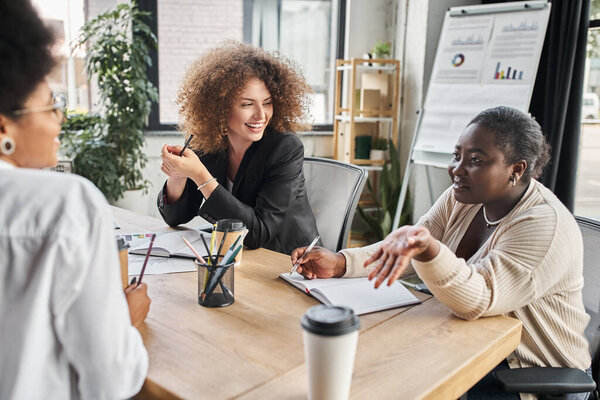 счастливые мультикультурные деловые женщины обсуждают стартап возле ноутбуков и кофе идти, творческая команда