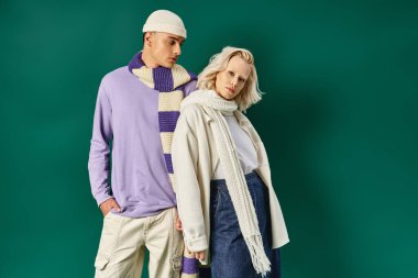 Kışın şık giyinen şık bir çift, kalın elbiseli bir adam, turkuaz arka planda genç bir kadının yanında poz veriyor.