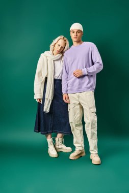 Uzun boylu, bereli yakışıklı bir adam. Sarışın bir kadınla kışın turkuaz arka planda poz veriyor.