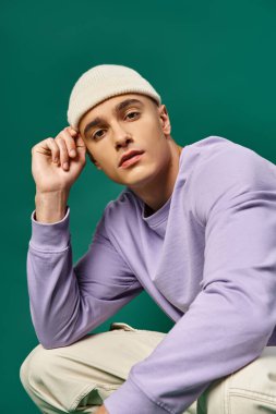 Mor kazaklı ve bereli yakışıklı bir adam turkuaz arka planda oturuyor, kış modasında.