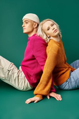 Kazaklı çift, sırt sırta oturan güzel kadın bereli adamla turkuaz arka planda.