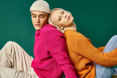 Güzel kadın bereli adamla sırt sırta oturuyor turkuaz arka planda, kış modasında.