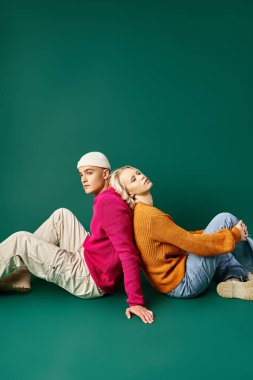 Güzel bir kadın bereli bir adamla sırt sırta oturuyor turkuaz arka planda, kış modasında.