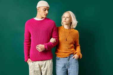 Kış kıyafetleri içinde şık bir çift. Turkuaz arka planda elleri ceplerinde poz veriyorlar.