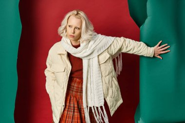 Beyaz kışlık ceketli şık bir kadın. Kırmızı arkaplanda el ele poz veriyor.