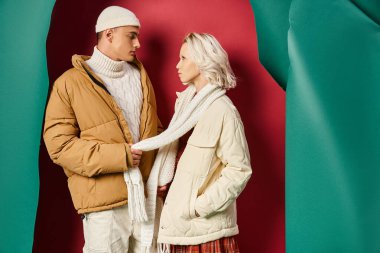 Sarışın, beyaz elbiseli, turkuaz yırtık saçlı, kırmızı arka planlı, eşarp takan ilgili bir adam.