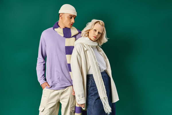 стильная пара в зимнем наряде, мужчина в теплой одежде позирует рядом с молодой женщиной на бирюзовом фоне