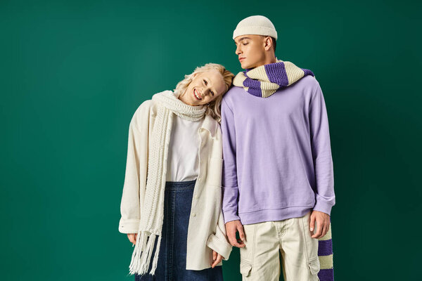 счастливая женщина в стильной зимней одежде кладет голову на плечо высокого мужчину на бирюзовом фоне