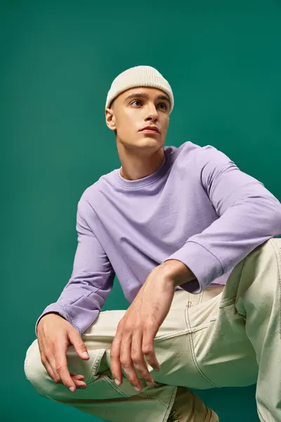 英俊潇洒的男子 身穿紫色运动衫 头戴便帽 坐在碧绿的背景上 冬季时尚 — 图库照片