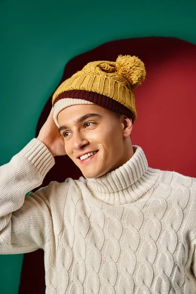 ターコイズの背景 冬の傾向に黄色のマスタードのボブル帽子を身に着けている白いセーターの幸せな男 — ストック写真