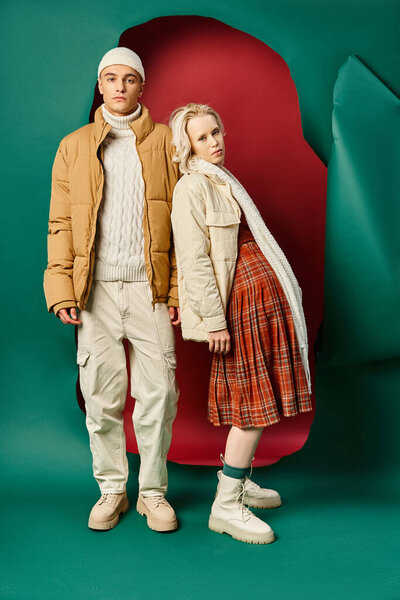 full length of couple in trendy winter jackets posing together on red with turquoise backdrop