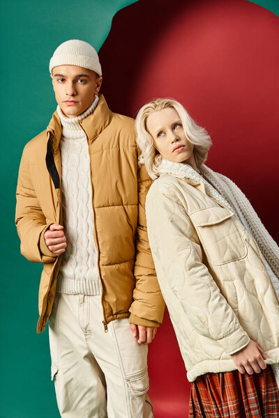 blonde woman in white winter jacket leaning on handsome man in beanie on red with turquoise backdrop