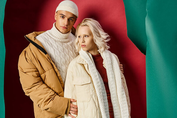 stylish man and woman in winter outerwear posing together on torn turquoise and red background