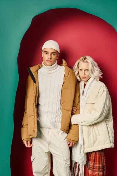白い冬のアウターウェアの金髪の女性は ターコイズと赤い背景の近くに男の手を保持しています — ストック写真