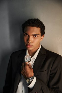 appealing young african american man in black elegant suit looking at camera on gray backdrop clipart