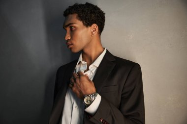 good looking young african american man with accessories in black suit posing and looking away clipart