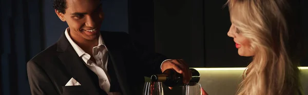 stock image joyful interracial young couple in evening attire preparing to drink red wine at home, banner