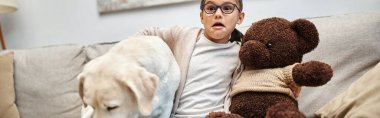 scared girl in eyeglasses holding teddy bear and sitting with labrador while watching movie, banner clipart