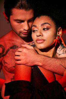 Yakışıklı dövmeli adam Afrikalı Amerikalı sevgilisine arkadan sarılıyor, seksi çift.