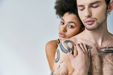 Genç, çekici Afrikalı Amerikalı kadın dövmeli erkek arkadaşına arkadan sarılıyor, seksi çift.