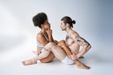 Hoş görünümlü, çok kültürlü, seksi, rahat iç çamaşırlı genç bir çift yerde birlikte oturuyor.