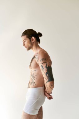 young good looking man with ponytail and cool tattoos in underwear posing on ecru background clipart