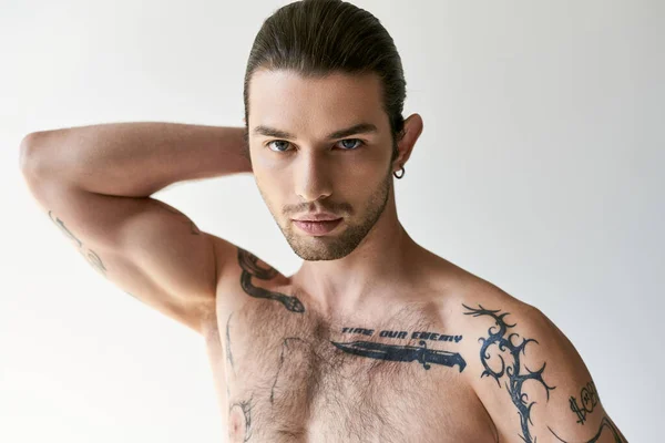 stock image young handsome man with ponytail and cool tattoos in comfy underwear posing on ecru background