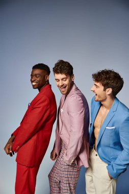 joyous handsome diverse men in stylish vibrant suits posing in single file on gray backdrop clipart
