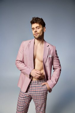 Düğmeleri açık pembe takım elbiseli yakışıklı bir adam. Gri arka planda poz veriyor. Moda konsepti.