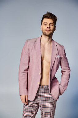 Düğmeleri iliklenmemiş, pembe takım elbiseli yakışıklı şık adam gri arka planda poz veriyor.