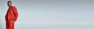 Gri arka planda poz veren parlak kırmızı elbiseli yakışıklı Afro-Amerikalı adam, moda konsepti, afiş
