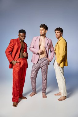 handsome multiracial friends in unbuttoned bright suits on gray background, fashion concept clipart