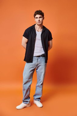 attractive young man in casual outfit on orange backdrop looking at camera, fashion concept clipart