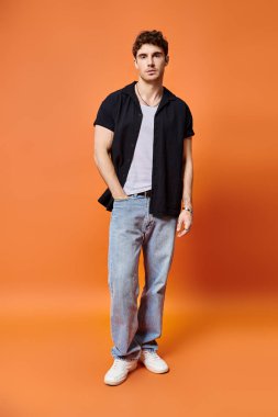 good looking young man in street outfit on orange backdrop looking at camera, fashion concept clipart