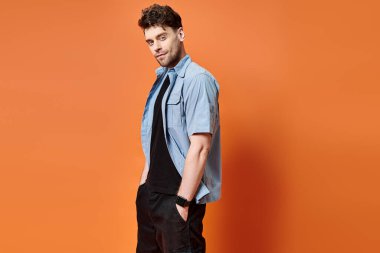 cheerful attractive man in casual outfit on orange backdrop looking at camera, fashion concept clipart