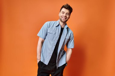 joyous attractive man in casual outfit on orange backdrop looking at camera, fashion concept clipart