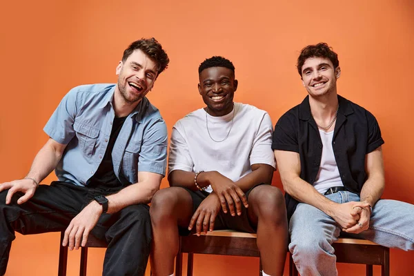 stock image cheerful diverse men in casual street outfits smiling happily on orange backdrop, fashion concept
