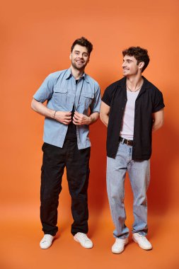 Şık sokak kıyafetleri içinde neşeli gençler turuncu arka planda birlikte poz veriyorlar, moda konsepti.
