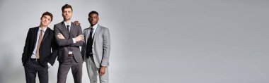 appealing interracial friends in smart business suits posing together on gray background, banner clipart