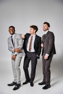 good looking happy interracial male models in smart suits smiling sincerely on gray backdrop clipart