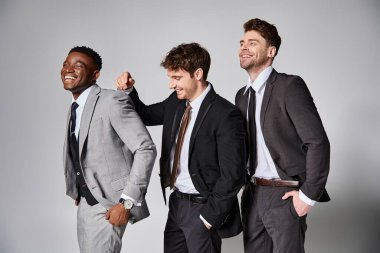 appealing happy multicultural male models in smart suits smiling sincerely on gray backdrop clipart