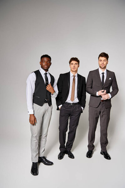 good looking young multicultural friends in smart business suits posing together on gray backdrop