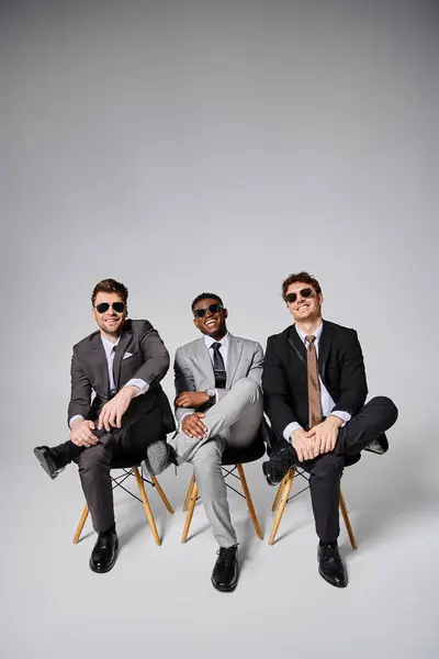 stock image cheerful young multicultural men in business smart suits sitting on chairs and smiling happily