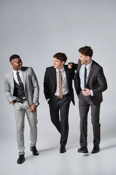 stock image good looking happy young diverse male models in smart suits smiling sincerely on gray backdrop